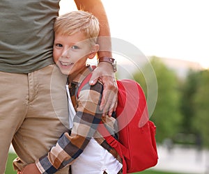 Happy little schoolboy hugging leg of his father on the way to school on 1st of September