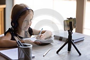 Happy little schoolgirl in headphones studying from home