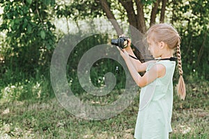 A happy little seven year old kid girl photographs a summer natural landscape with a camera using live view. children adopt their