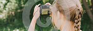 A happy little seven year old kid girl photographs a summer natural landscape with a camera using live view. children adopt their