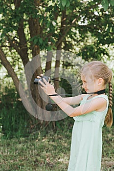 A happy little seven year old kid girl photographs a summer natural landscape with a camera using live view. children adopt their