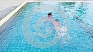 Happy little sisters are swimming and playing in outdoor swimming pool in a tropical resort during family summer vacation. Kids le