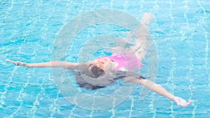 Happy little sisters are swimming and playing in outdoor swimming pool in a tropical resort during family summer vacation. Kids le