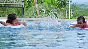 Happy little sisters are swimming and playing in outdoor swimming pool in a tropical resort during family summer vacation. Kids le