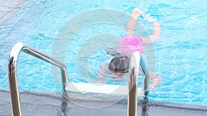 Happy little sisters are swimming and playing in outdoor swimming pool in a tropical resort during family summer vacation. Kids le