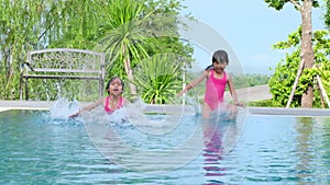 Happy little sisters are swimming and playing in outdoor swimming pool in a tropical resort during family summer vacation. Kids le