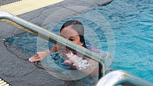 Happy little sisters are swimming and playing in outdoor swimming pool in a tropical resort during family summer vacation. Kids le