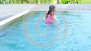 Happy little sisters are swimming and playing in outdoor swimming pool in a tropical resort during family summer vacation. Kids le