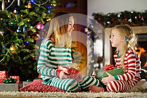 Happy little sisters wearing Christmas pajamas playing by a fireplace in a cozy dark living room on Christmas eve.