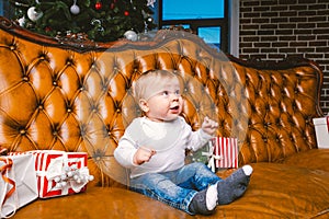 Happy little smiling boy with christmas gift box. Beautiful little baby, sits on asofa with gift. Child sitting by a