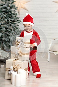 Happy little smiling boy in santa claus costume holds white christmas gift box