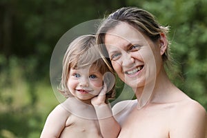 Happy little smiling child in the arms of the mother on a natural