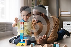 Happy little son playing with black dad using wooden blocks