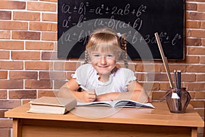 Happy little student girl sitting at a school desk and studying math. The child is doing homework. Preschool education, self