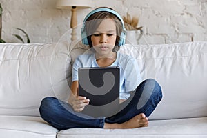 Happy little teenage boy in headphones using tablet.