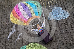 Happy little toddler girl flying in hot air balloon painted with colorful chalks in rainbow colors on ground or asphalt