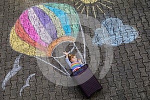 Happy little toddler girl flying in hot air balloon painted with colorful chalks in rainbow colors on ground or asphalt