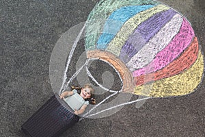 Happy little toddler girl flying in hot air balloon painted with colorful chalks in rainbow colors on ground or asphalt