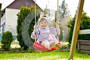 Happy little toddler girl having fun on swing in domestic garden. Smiling positive healthy child swinging on sunny day