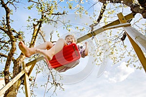 Happy little toddler girl having fun on swing in domestic garden. Smiling positive healthy child swinging on sunny day