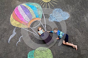 Happy little toddler girl and kid boy flying in hot air balloon painted with colorful chalks in rainbow colors on ground
