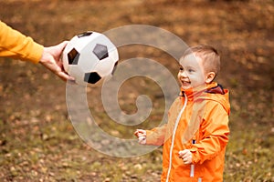 Happy little toddler kid watching at soccer ball in hand of father. Hand of dad giving to little son football ball in autumn park