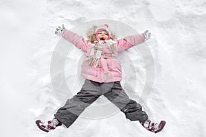 A happy little toothless girl in the winter walk, in the nature. A child making an angel on the snow