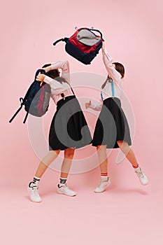 Happy little twin schoolgirls fighting with their backpacks. Low angle