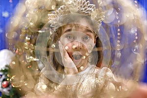 Happy little 10 years girl looking at camera through a christmas ball in festive  decorated home interrior