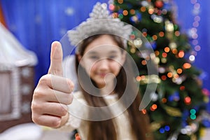 Happy little 10 years girl show thumb up, sign ok, looking at camera in christmas decorated home indoor