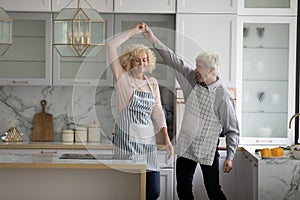 Happy lively older couple dancing in cozy kitchen