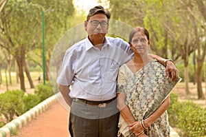 Happy looking retired senior Indian man and woman couple smiling and posing in a park outdoor setting in New Delhi, India. Concept