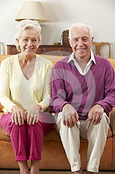 Happy Looking Senior Couple Sitting On Sofa At Home