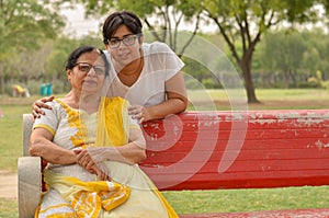 Happy looking young Indian woman with her mother sitting on a red bench in a park in New Delhi, India. Concept Mother`s day