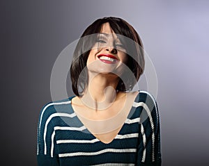 Happy loudly laughing with wide smile young woman with short hair in fashion sweater. portrait on grey background