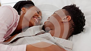 Happy, love and couple in a bedroom laughing and bonding while lying together at home. Young black man and woman on a