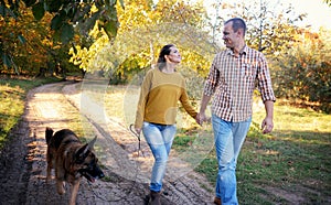 Happy love couple walking in park with german shepherd dog, holding hands and look each other