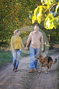 Happy love couple walking in park with their german shepherd dog, holding hands