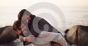 Happy, love and young couple playful back ride, smile or laugh on the beach during sunset. Portrait of man and woman on