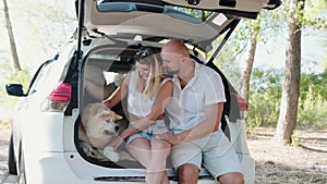 Happy lovely couple with Akita Inu sitting in the open trunk car