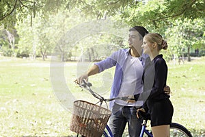 Happy lovely young couple with bike walking in the garden  spending time together. Lover going on a picnic in summer park and