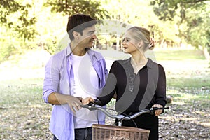 Happy lovely young couple with bike walking in the garden  spending time together. Lover going on a picnic in summer park and