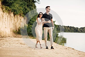 Happy lovers at the beach near lake. Young couple is holding hands and walking on summer day outdoors. A man and woman in love.