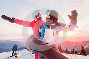 Happy lovers couple man and young women snowboarders on background of ski resort sunset. Concept winter sports Alps