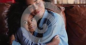 Happy loving affectionate african american mother cuddling small daughter.