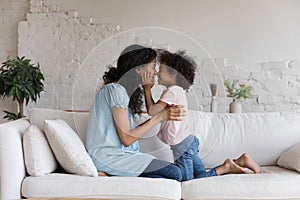 Happy loving African American mother kissing adorable preschool daughter