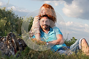 Happy loving attractive couple laying by bonfire hugging in grass and clouds. Couple loves picnic outside city