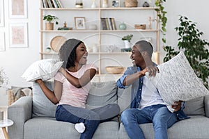 Happy loving black couple fighting with pillows in living room