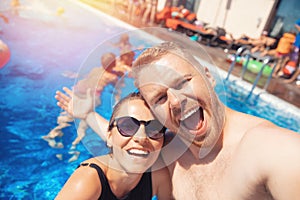 Happy loving couple Caucasian man and woman hugging and making selfie photo on background of pool. Smile and tanned skin