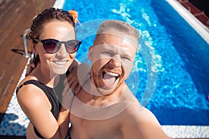 Happy loving couple Caucasian man and woman hugging and making selfie photo on background of pool. Smile and tanned skin